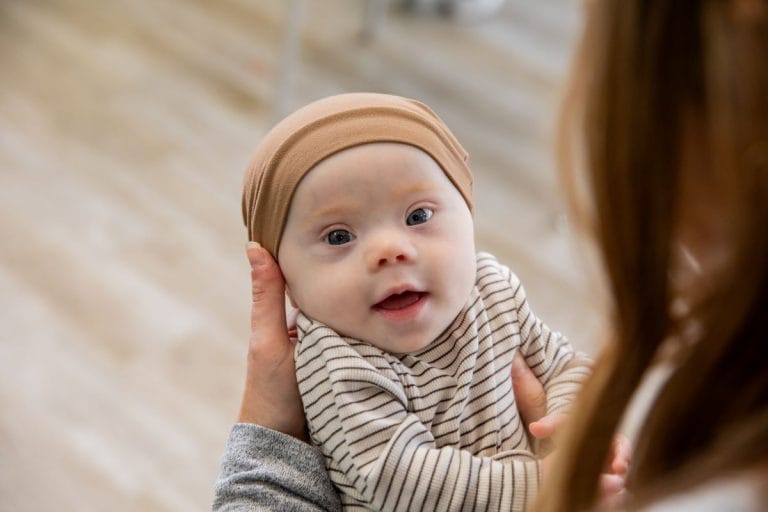 Pipopäinen down-vauva hymyilee vanhemman sylissä