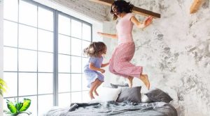 Äiti ja pieni tytär hyppivät sängyllä valoisassa huoneessa.