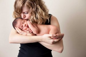 Nuori äiti suukottaa sylissään makaavaa pientä, alastonta vauvaa.
