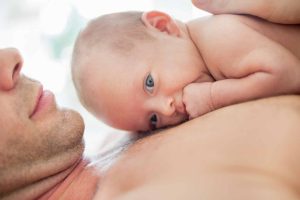 Pieni vauva makoilee ihokontaktissa isän rintakehän päällä.