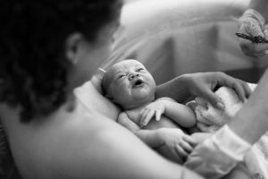 Vastasyntynyt vauva lepää juuri synnyttäneen vanhemman käsivarsilla synnytysaltaassa.