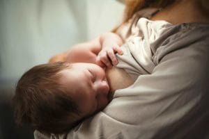 Äiti imettää tummahiuksista pientä vauvaa.