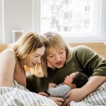 Vauvan kaksi äitiä ihailevat vauvaa aamulla sängyssä.