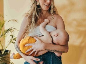 Iloinen vanhempi imettää lasta, joka nappaa kädellään hänen hiuksistaan otteen.