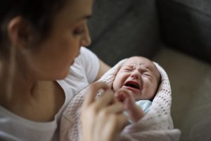 Vanhempi rauhoittelee sylissään vilttiin käärittyä, itkevää vauvaa.