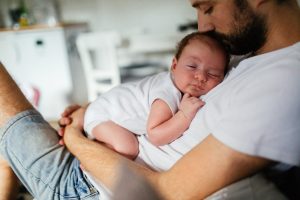 Parrakas vanhempi suukottaa vatsan päällä nukkuvan vauvan päätä.