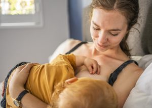 Vanhempi imettää keltapaitaista taaperoa ja hymyilee lapselle