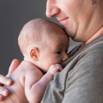 Hamuileva vastasyntynyt on hymyilevän isän sylissä