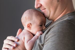 Hamuileva vastasyntynyt on hymyilevän isän sylissä