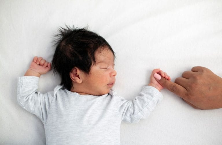 Mustatukkainen vastasyntynyt nukkuu selällään ja pitää aikuista sormesta kiinni